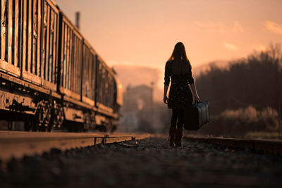 Rear view of woman standing on train at sunset