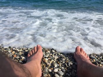 Low section of man sitting on pebbles at beach