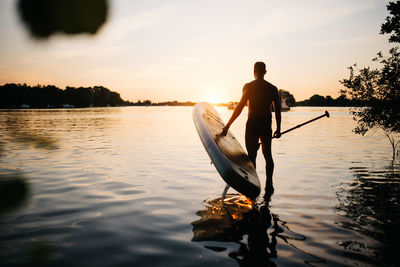 Silhouette man standing on lake against sky during sunset