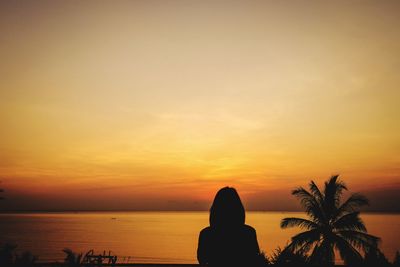 Silhouette person by sea against sky during sunset