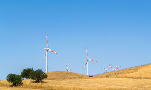 Windmill on field against clear blue sky