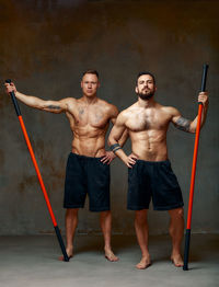Full length muscular men standing against wall