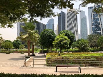 Park bench by buildings against sky in city