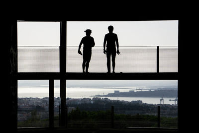 Silhouette men standing on walkway against sky