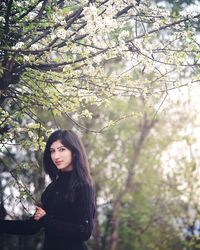 Portrait of young woman standing against tree