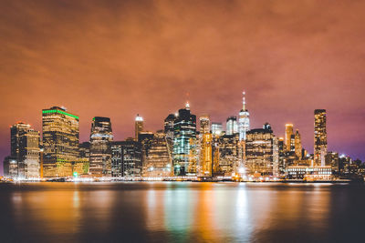 Illuminated buildings by river against sky in city at night