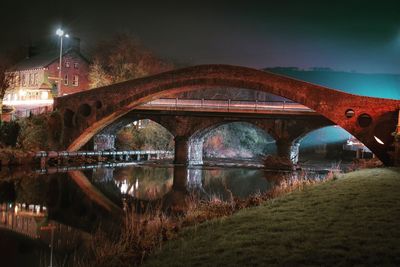 Arch bridge over river against sky at night