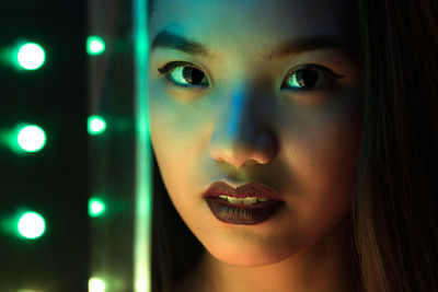 Close-up portrait of young woman by illuminated lights