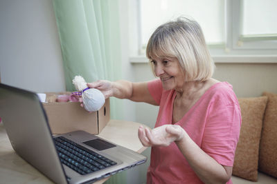 Senior woman holding gift while using laptop at home
