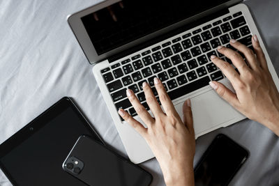 Cropped hands of woman using laptop on bed