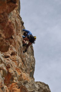 Low angle view of person rock climbing against sky