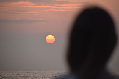 Silhouette person by sea against sky during sunset