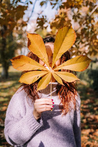 Smiling woman holding autumn leaf at park