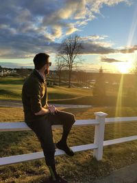 Side view of man standing by railing against sky during sunset