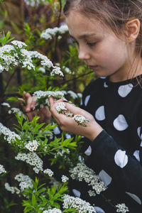 Cute girl holding flowering plant while standing outdoors