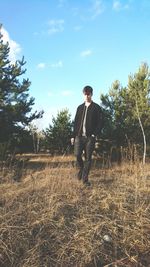 Full length of young man standing on grassy field against sky