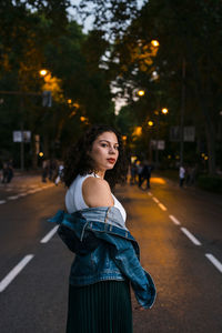 Portrait of young woman standing on road in city