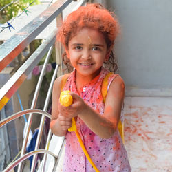 Sweet little indian girl playing colours on holi festival, holding pichakaree full of colours