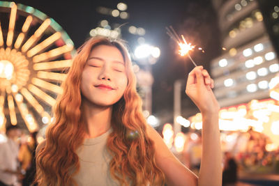 Young woman holding illuminated sparklers at night