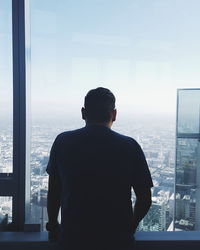 Rear view of man looking through window in city