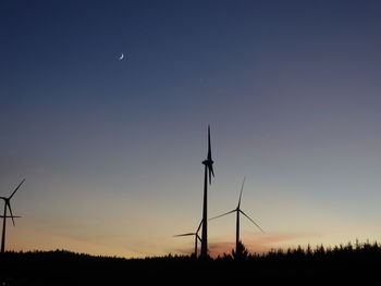 Silhouette wind turbines on field against sky during sunset