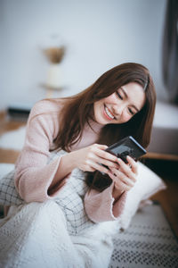Young woman using mobile phone while sitting on laptop