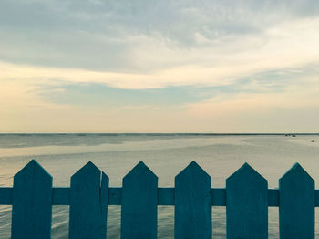 Wooden fence by sea against sky