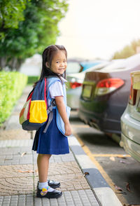 Portrait of cute smiling girl wearing school uniform standing on footpath
