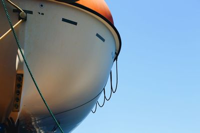 Low angle view hanging lifeboat against clear blue sky