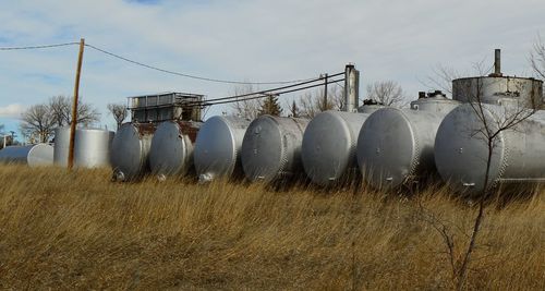 Silver storage tanks on grassy field against sky
