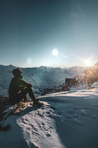 Man sitting on snowcapped mountain against sky during winter