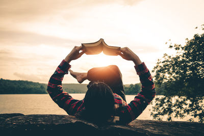 Midsection of woman sitting on shore against sky during sunset