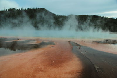 Grand prismatic spring steam rising as the pool runs off into orange and black thermophiles.