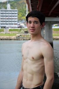 Portrait of shirtless young man standing outdoors by river