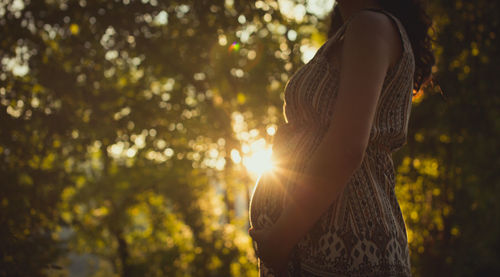 Midsection of pregnant woman standing against trees