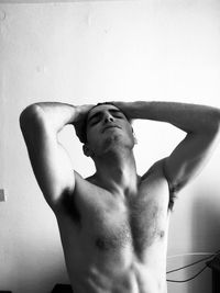 Young shirtless man with head in hand against wall