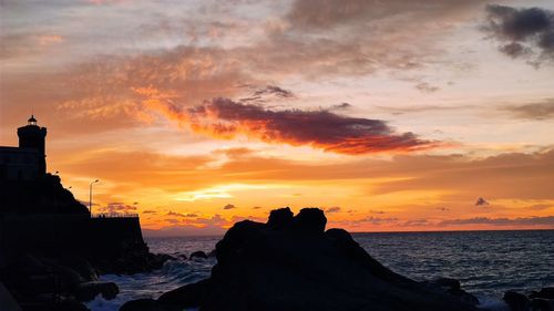 Silhouette rocks by sea against sky during sunset