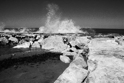 Waves splashing on shore against clear sky