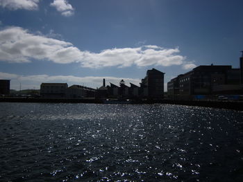 Buildings by river against sky in city