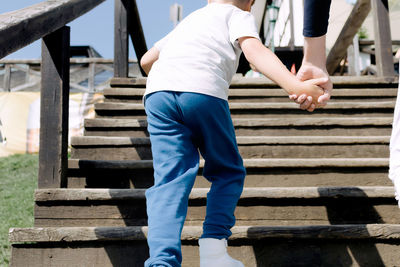 Rear view of boy holding father's hand while walking up the stairs outdoors.
