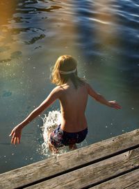 Rear view of shirtless boy jumping to lake