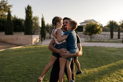 Father carrying daughter and son in arms while standing at park