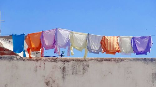 Low angle view of multi colored clothesline hanging on building terrace against clear blue sky