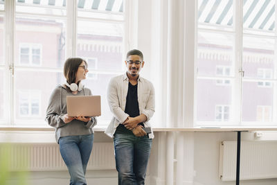 Smiling computer programmers talking while standing by desk in office