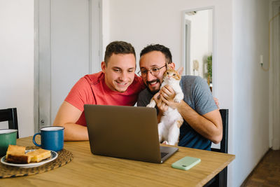 Two men and a cat looking at a laptop.