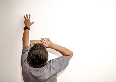 Rear view of teenager boy holding cardboard box and touching wall