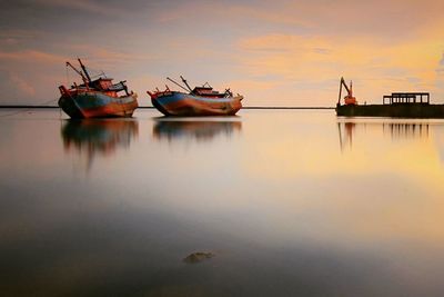 Fishing boats in lake against sky during sunset