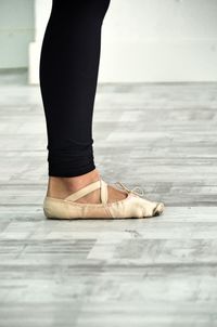 Low section of woman wearing ballet shoe standing on floor