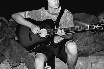 Midsection of man plying guitar while sitting by plants at night