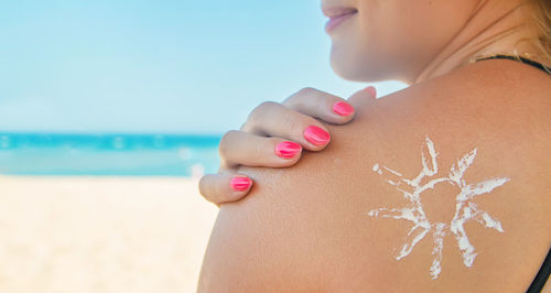 Close-up of woman with hand on beach against sky